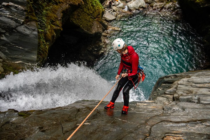 Person in helmet rappelling down a waterfall in a rocky gorge.