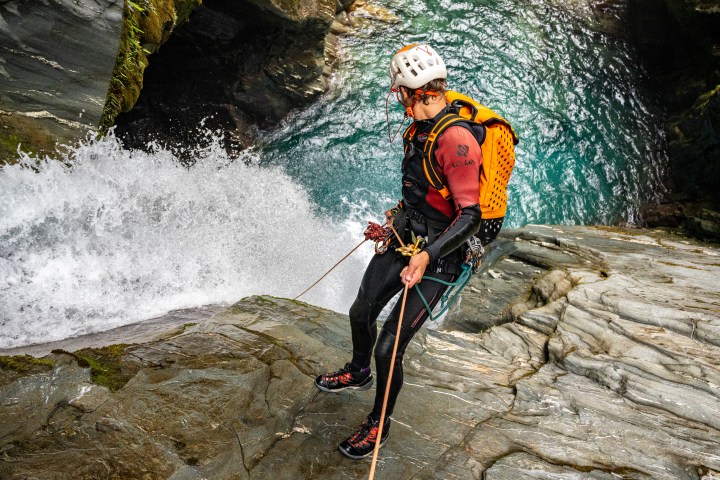 Person in gear rappelling down waterfall on rocky cliff.