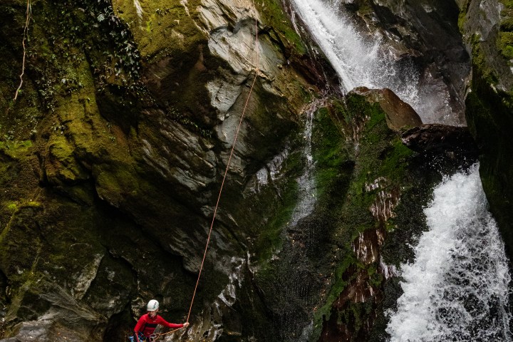 Person in gear rappelling down a waterfall in a rocky canyon.