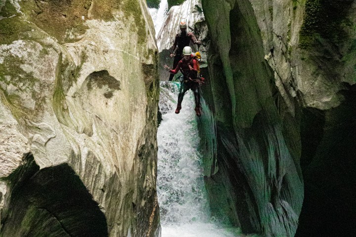 Two people canyoning down a waterfall between steep, rocky cliffs.
