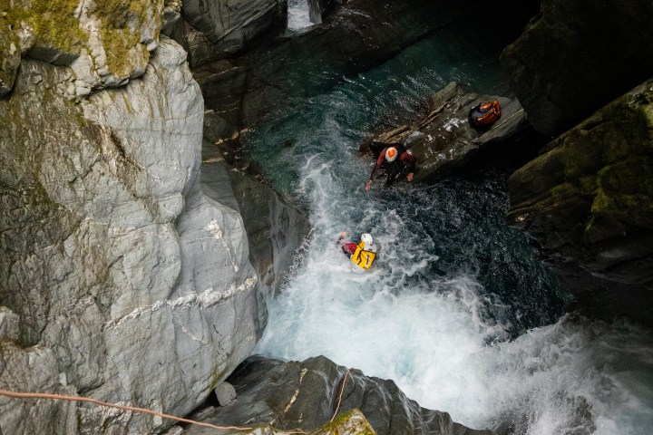 Person in yellow suit canyoning through a narrow rocky gorge with rushing water.