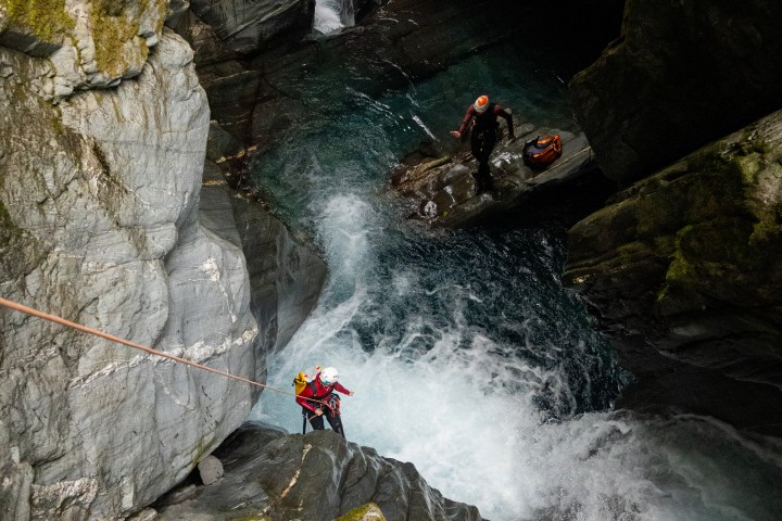 Two people canyoning in a rocky, water-filled gorge.