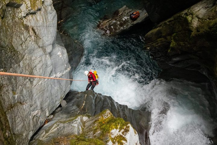 Person canyoning down a waterfall in a rocky gorge with safety gear.