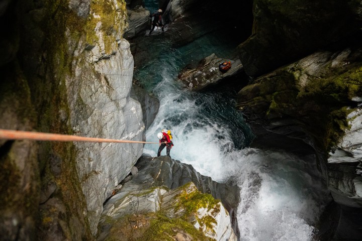 Person rappelling down waterfall in rocky terrain with safety gear.