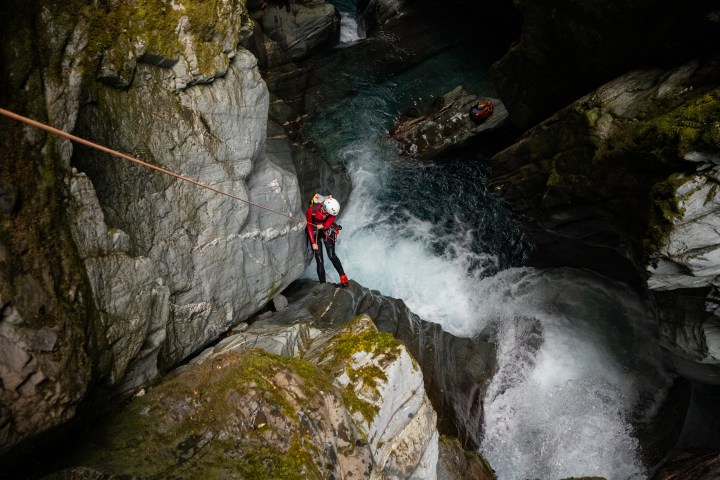 Person in red gear rappels down rocky waterfall canyon.