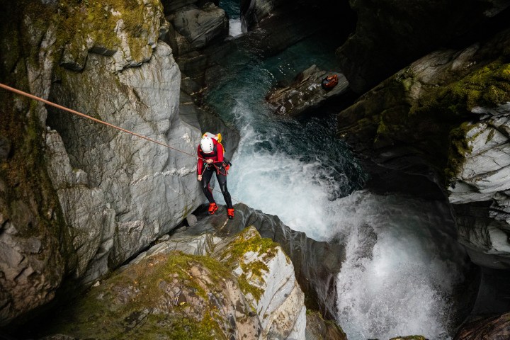 Person in climbing gear rappelling down rocky canyon near rushing water.