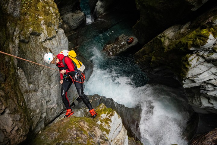 Person canyoning down a rocky waterfall wearing a helmet and wetsuit.