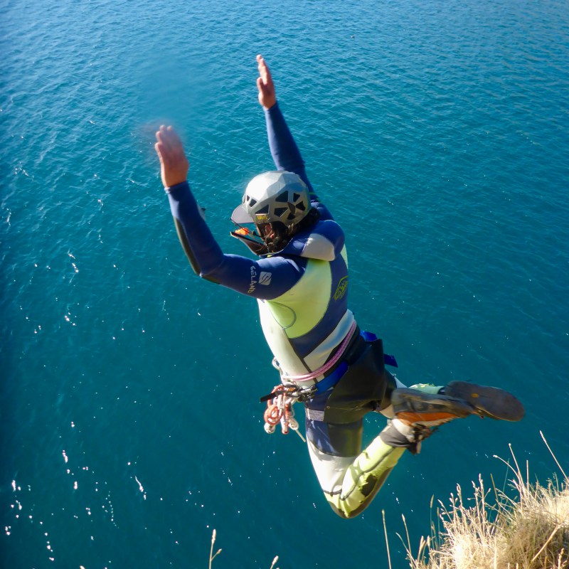 Person in helmet and wetsuit jumping off a cliff into the sea.