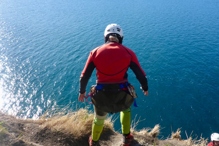 Person in wetsuit and helmet preparing to jump off cliff into water.