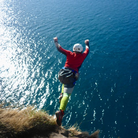 Person cliff jumping into blue water, wearing a helmet and gear.