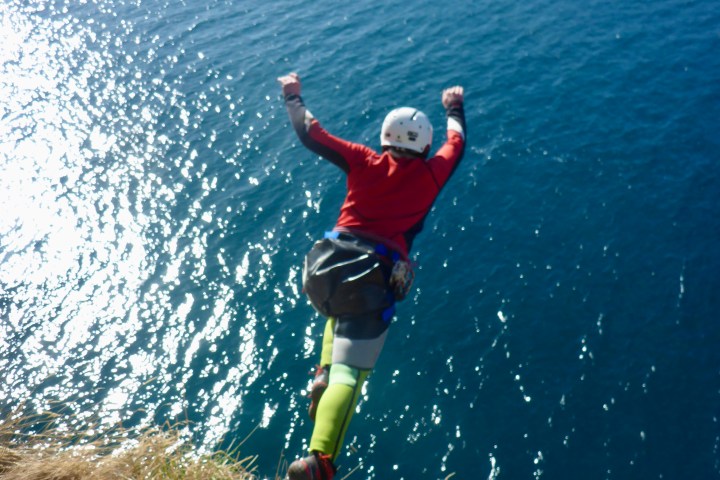 Person cliff jumping into blue water, wearing a helmet and gear.