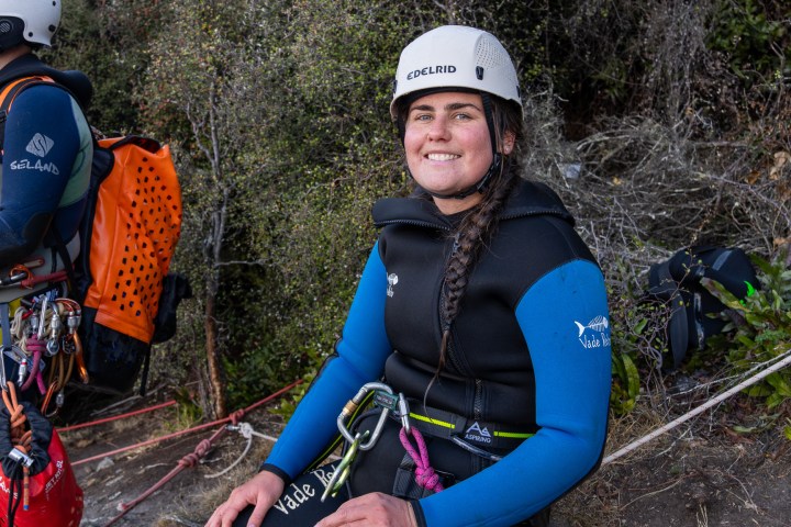 Person in helmet with climbing gear sitting outdoors, smiling.