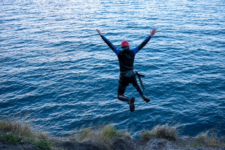 Person in wetsuit and helmet jumps into ocean from cliff.