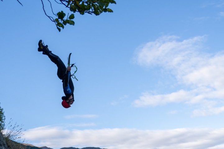 Person in wetsuit mid-air during cliff jump over water.