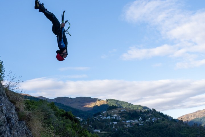 Person in wetsuit mid-air during cliff jump over water.