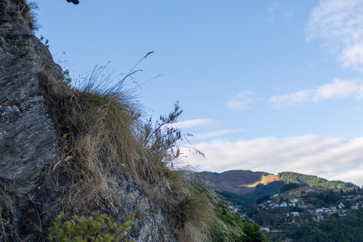 Person in mid-air jumping from cliff over water with hills in the background.