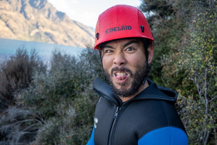 Man in a red helmet making a funny face outdoors by a lake.