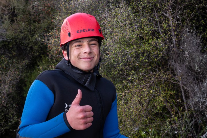 Person in red helmet and blue wetsuit giving thumbs up outdoors.