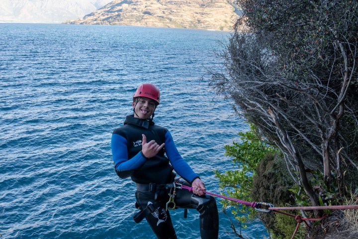 Person in wetsuit and helmet rappelling near a body of water.