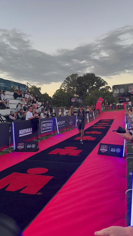 Triathlete running on red carpeted path with spectators clapping on both sides at an outdoor event.