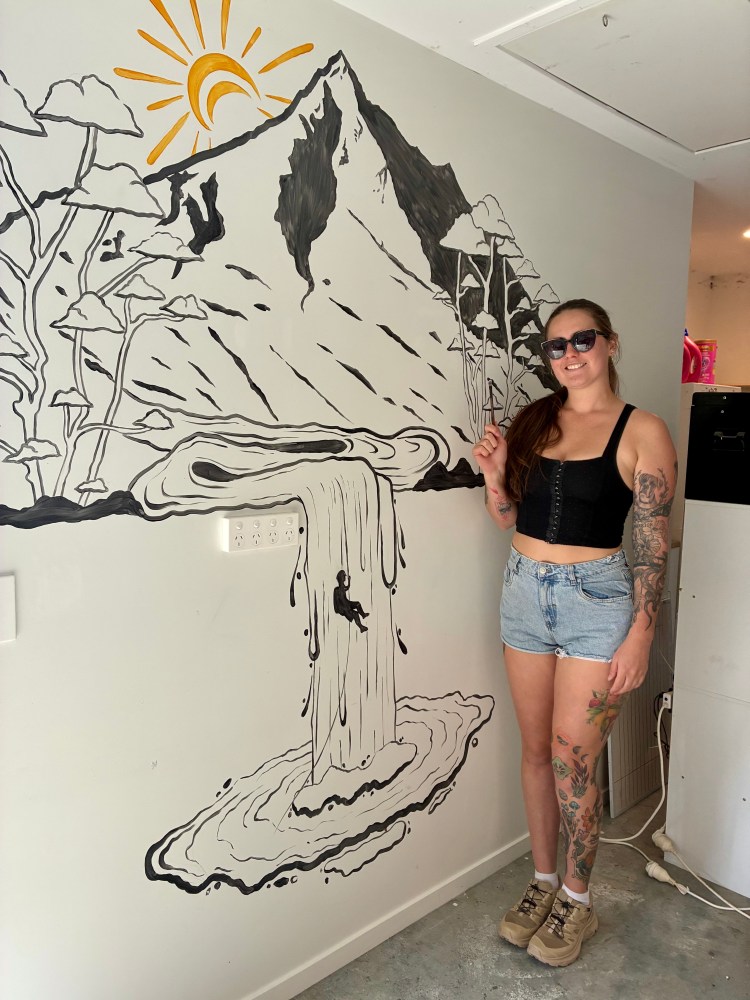 Kaylah standing beside her mural at the canyoning nz base