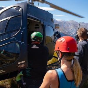 People boarding a helicopter on a grassy area with mountains in the background.