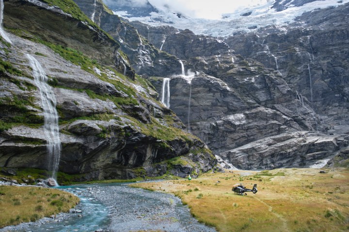Helicopter landed in a rocky mountain valley with waterfalls and a winding stream.