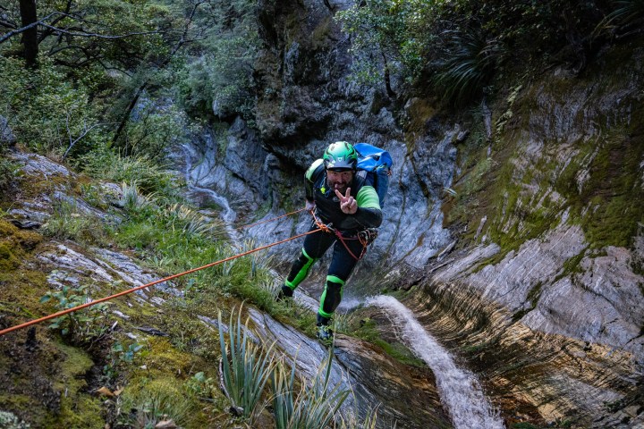 Person rappelling down a rocky canyon with a rope, surrounded by lush greenery.