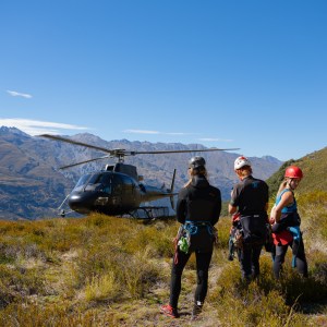 Helicopter landing near people in hiking gear on a grassy mountain.