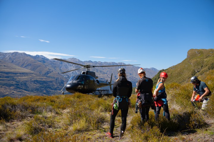 Helicopter landing near people in hiking gear on a grassy mountain.