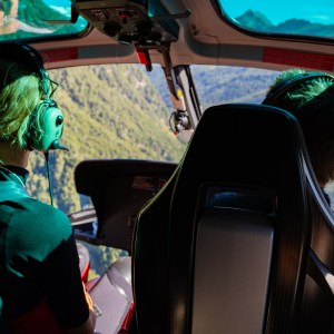 People inside a helicopter with a view of mountains through the windshield.