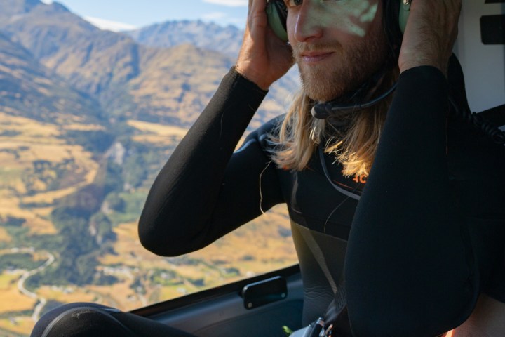 Person in helmet sitting in helicopter with mountain view outside.