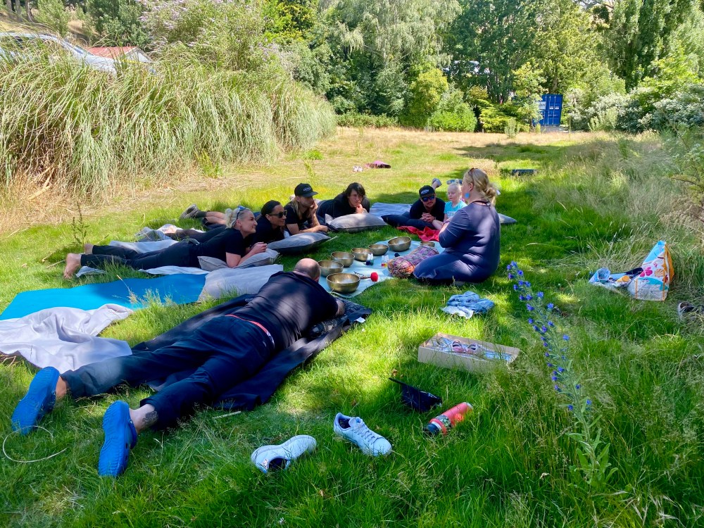 Group relaxing on grass outside with sound bowls in a circle.