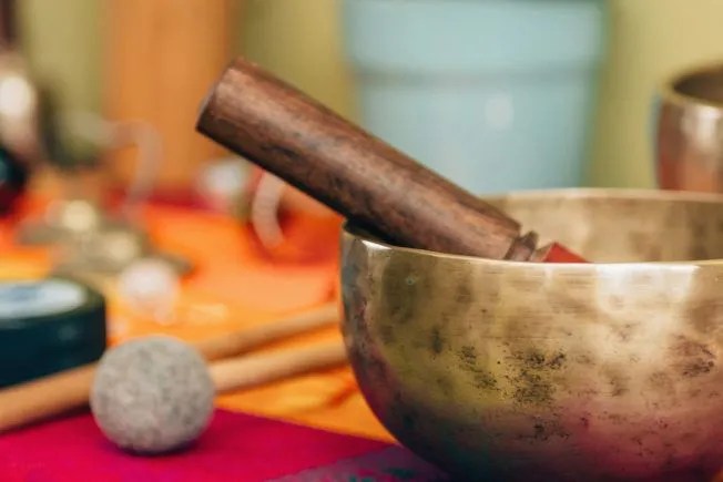 Brass singing bowl with wooden mallet on colorful fabric.