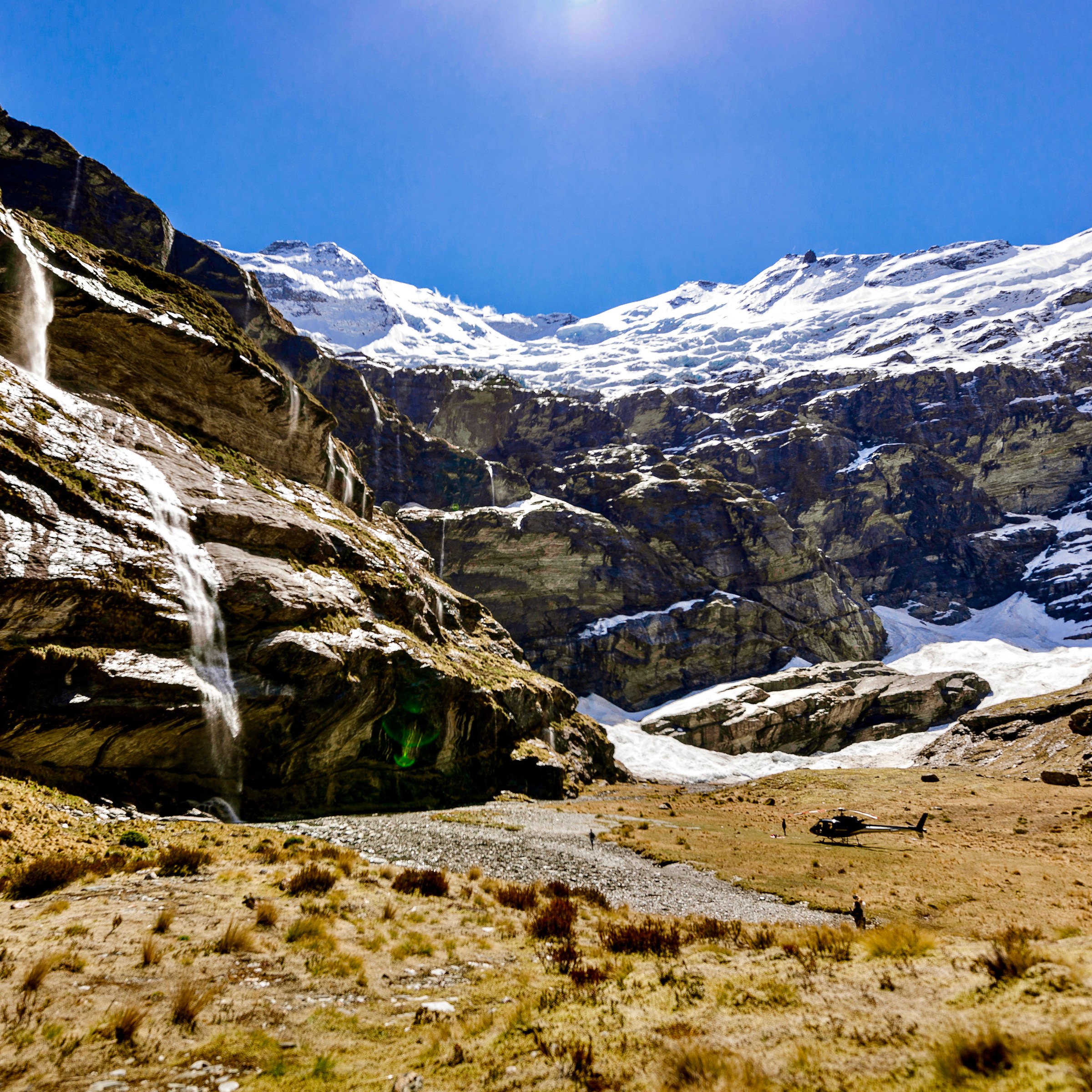 Mountain landscape with waterfall, snowy peaks, and a rocky valley.