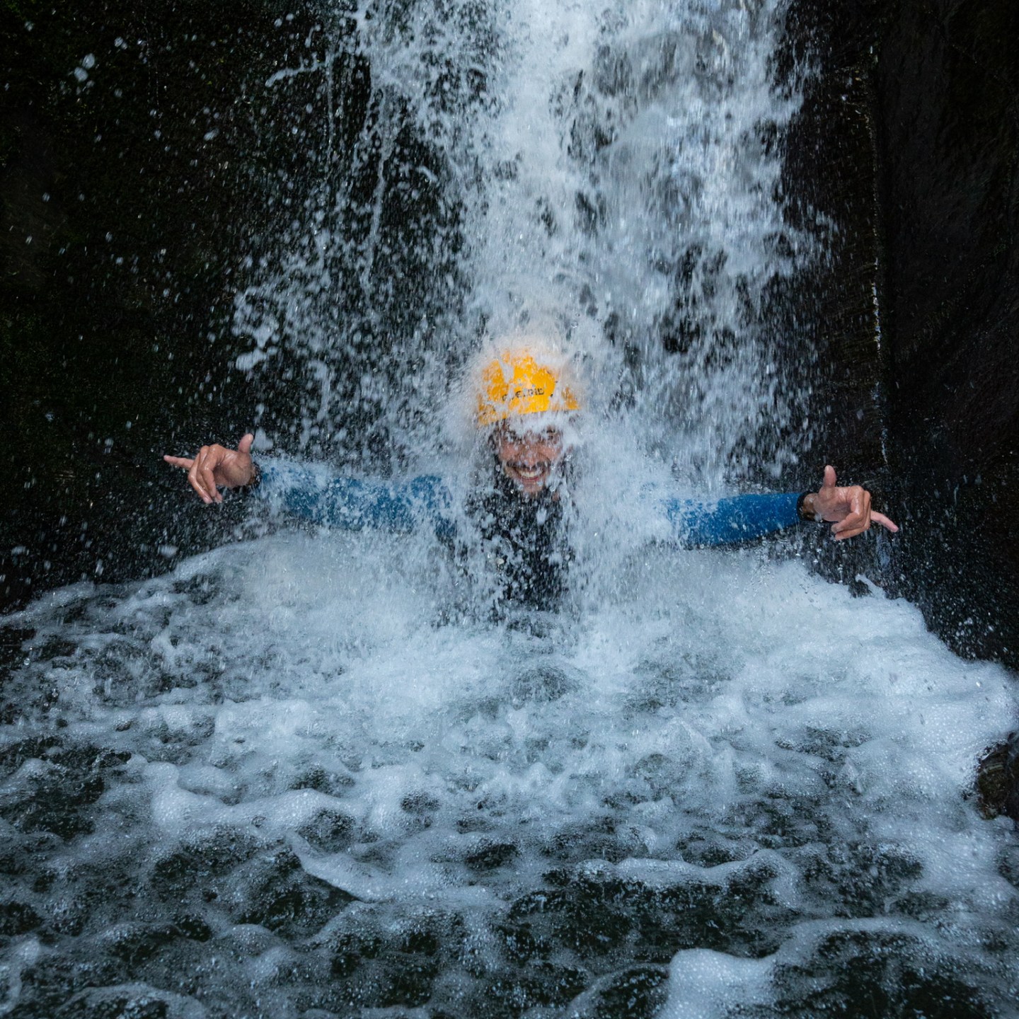 Person in yellow helmet enjoying waterfall splash