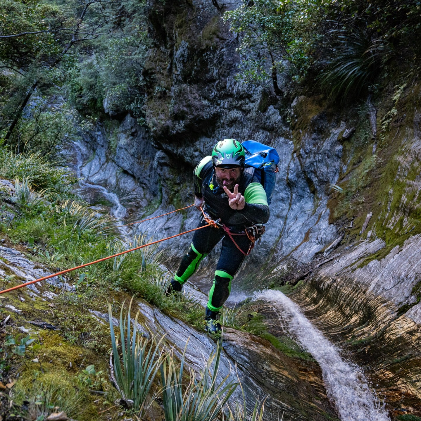 Person in wet suit rappelling down a rocky waterfall in a forested area.