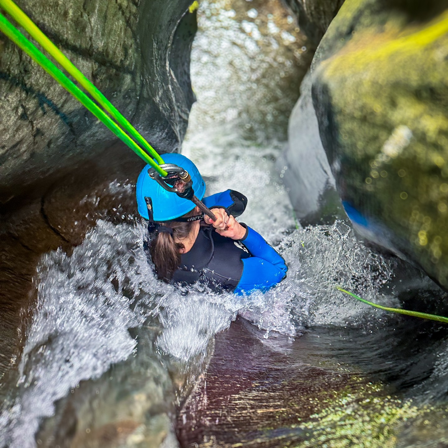 Person in wetsuit and helmet canyoning through narrow water passage.