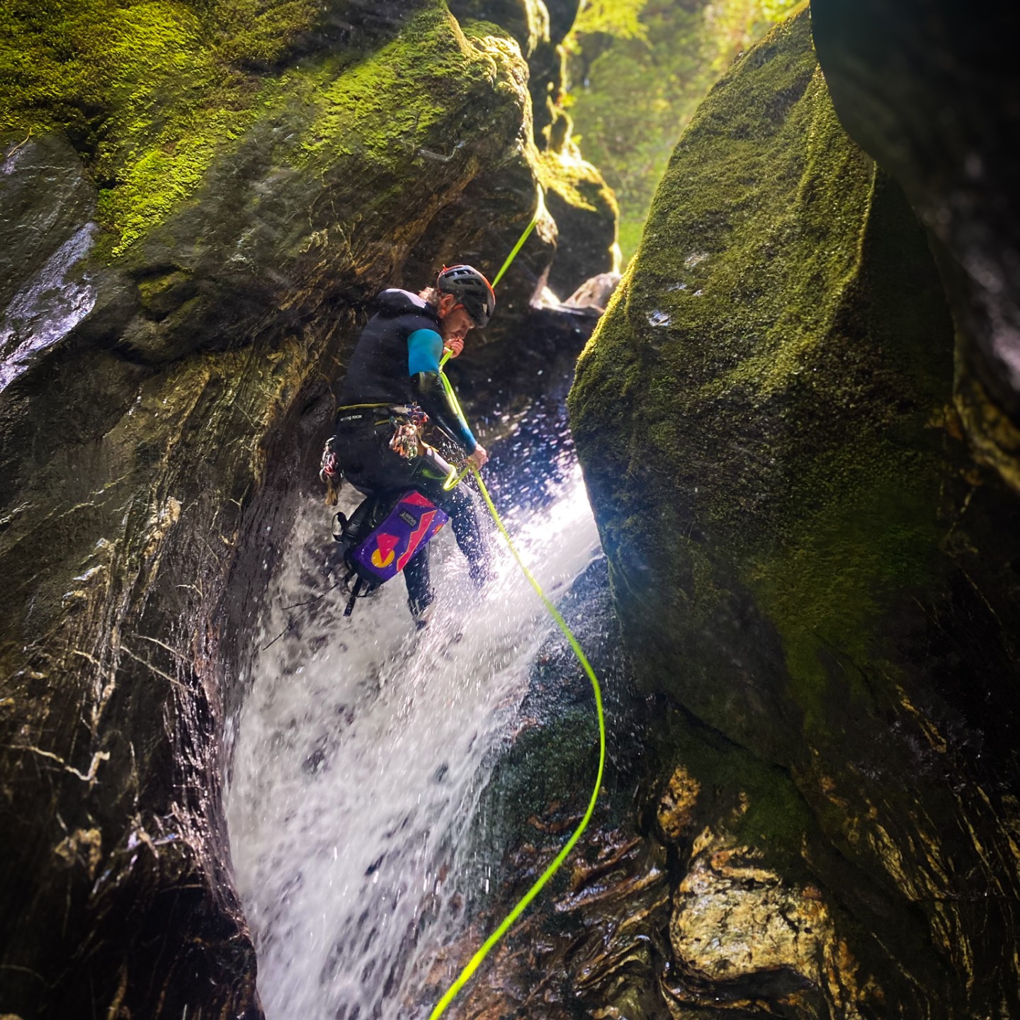 Person canyoning down a waterfall in a mossy, rocky canyon.