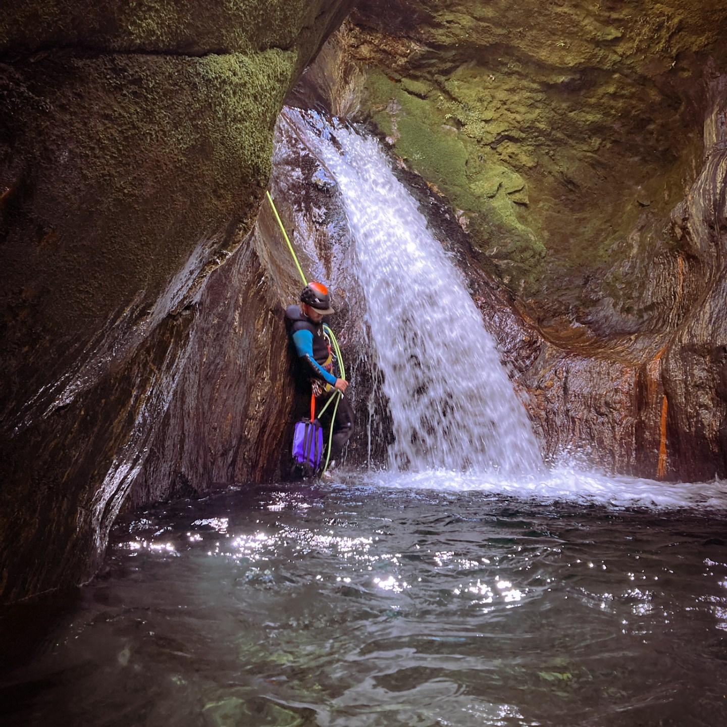 Person in wetsuit canyoning near a small waterfall in rocky environment.