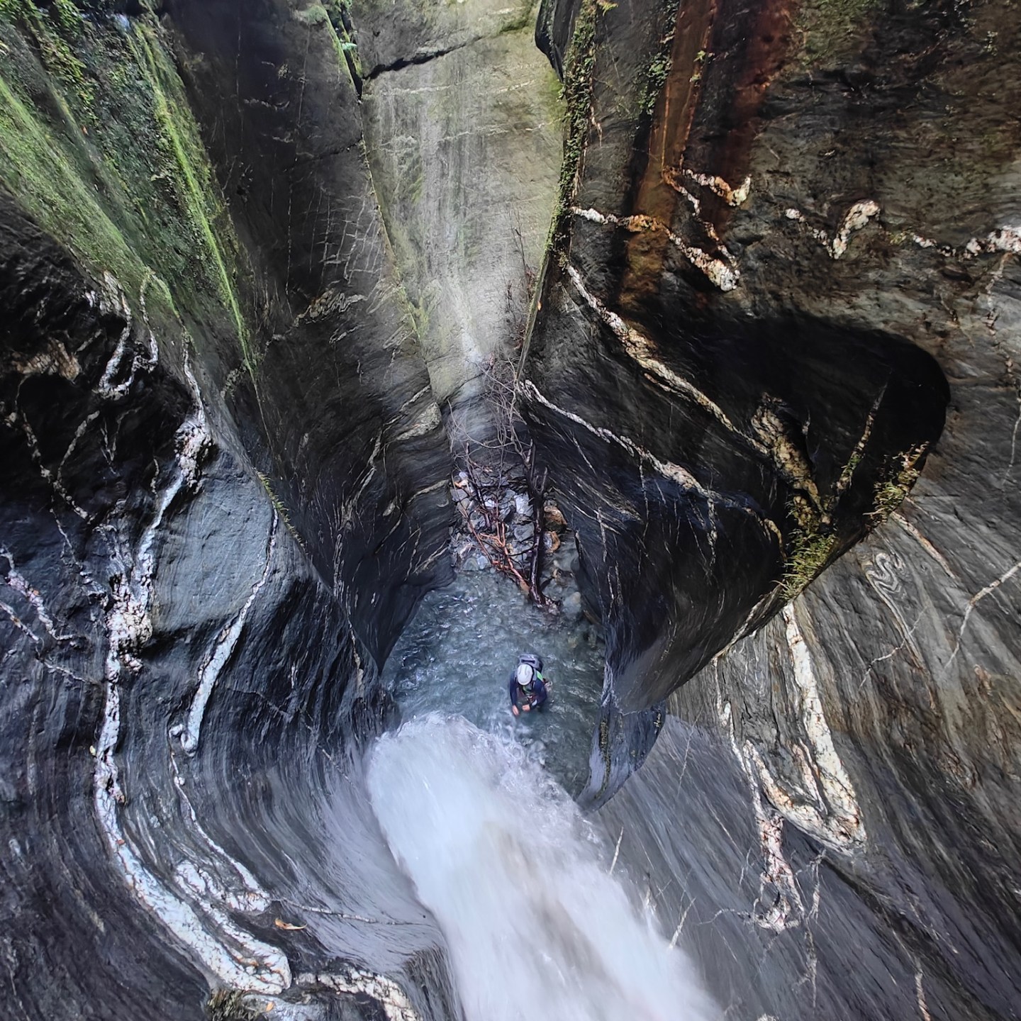 Person descending into a narrow rock canyon with rushing water.