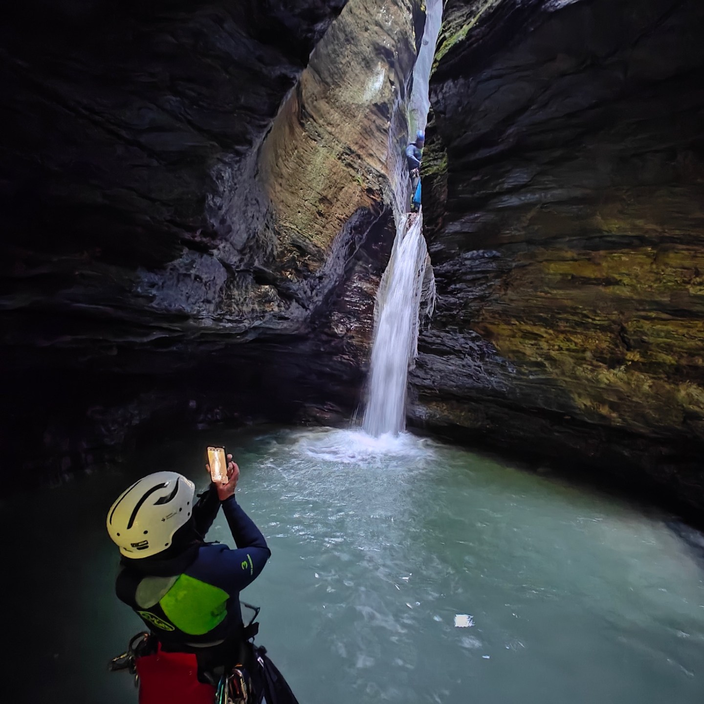 Person in canyon taking photo of waterfall and climber.