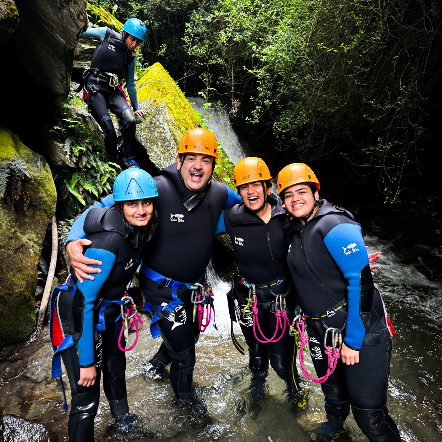 Group in helmets and wetsuits smiling at a forest stream.