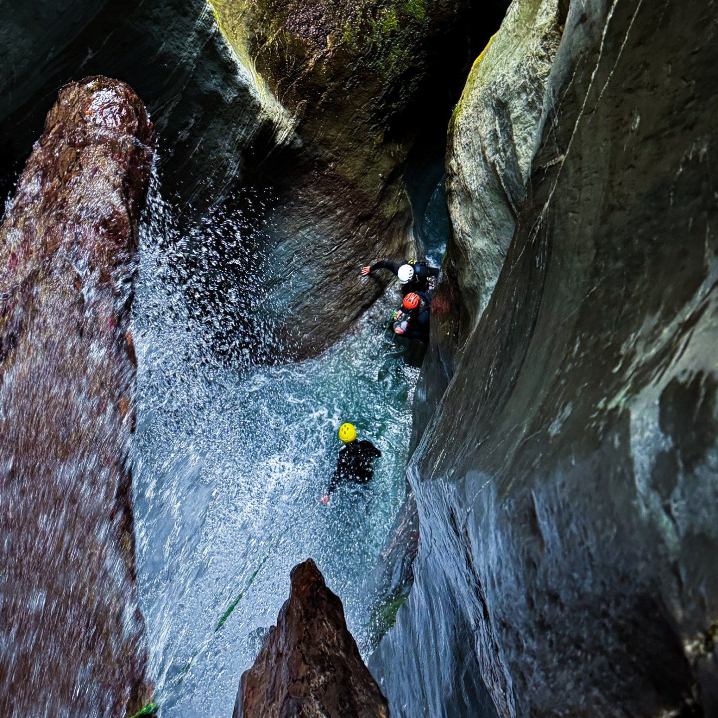 People canyoning between narrow rock walls with waterfall splashing.