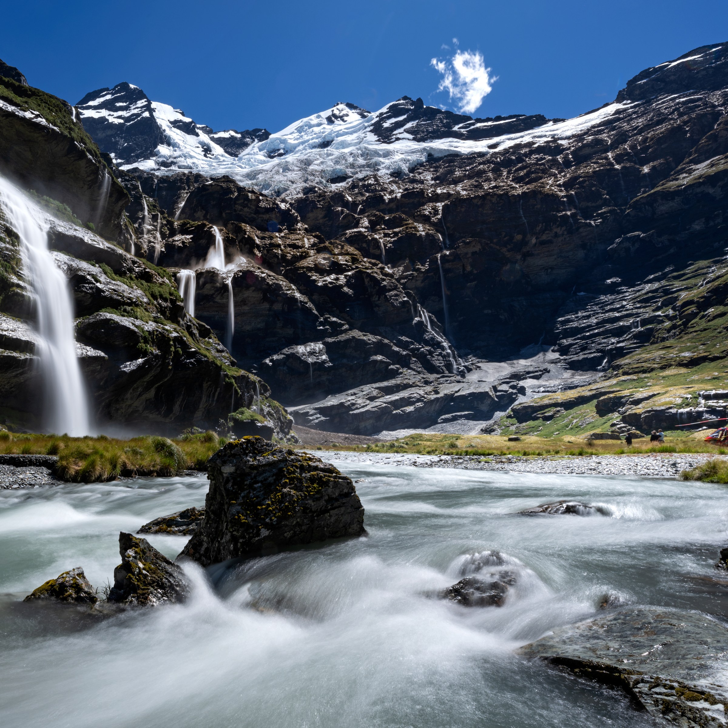 Mountain landscape with waterfalls and a river under a blue sky.