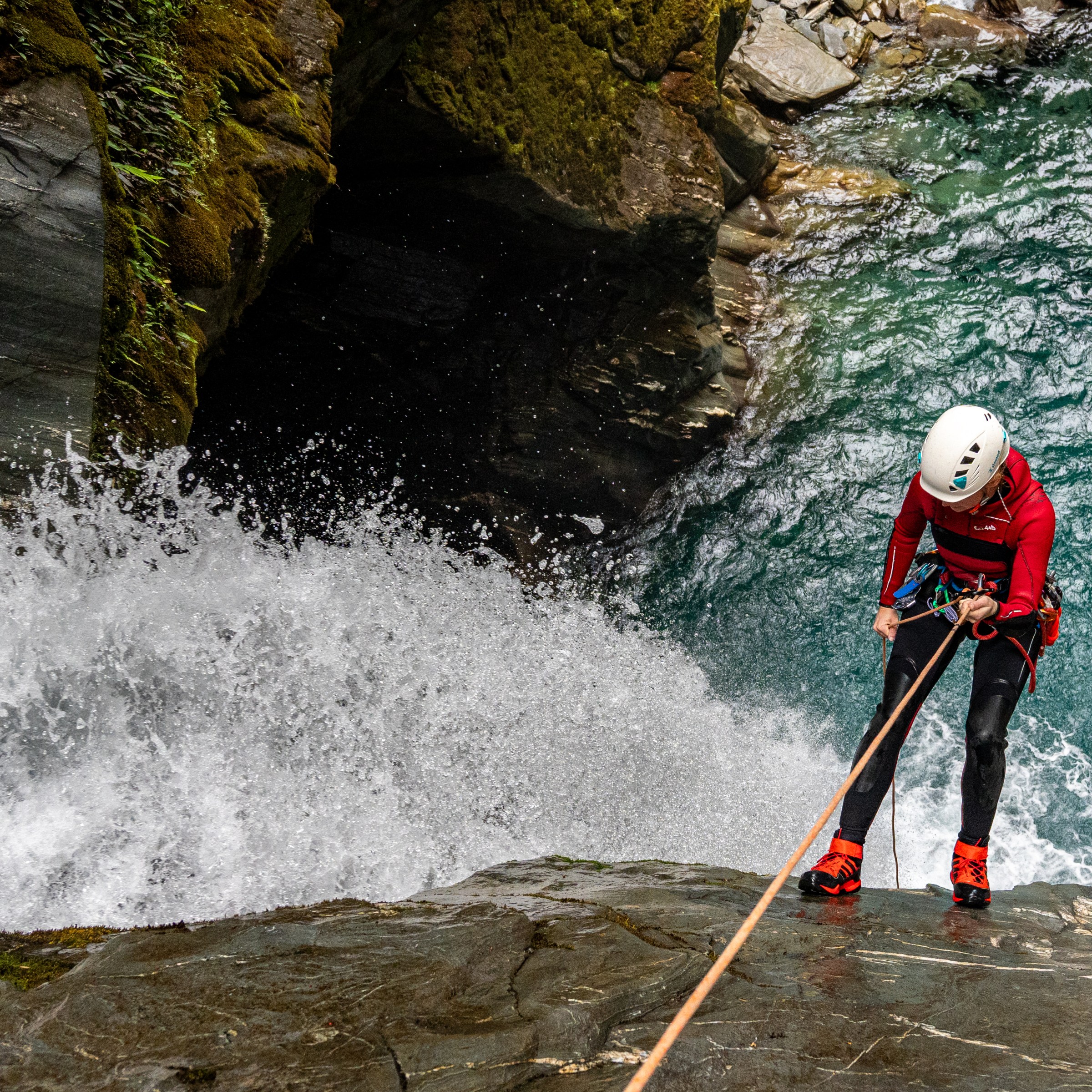 Person in helmet rappelling down a waterfall into a rocky pool.