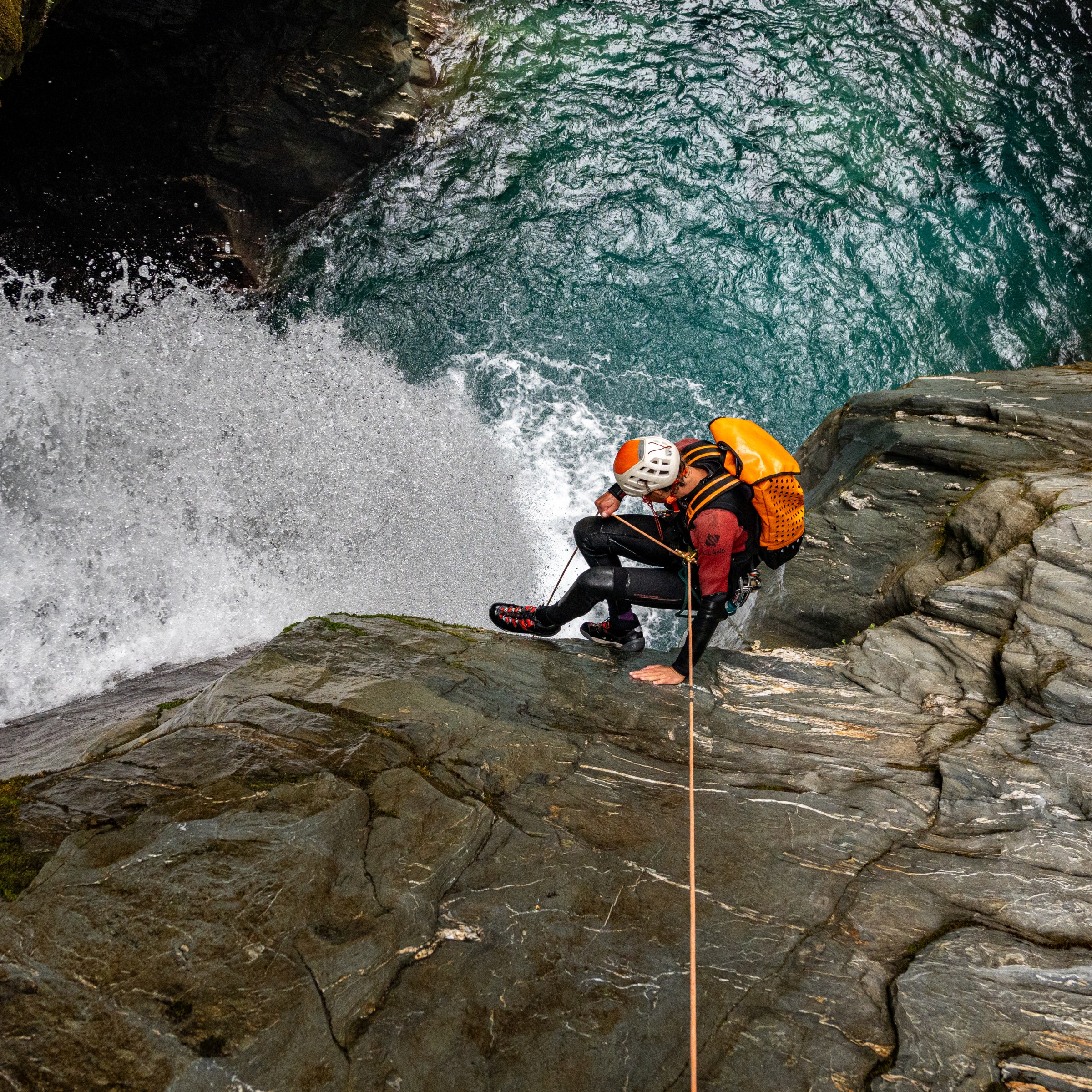 Two climbers descending a rocky waterfall with safety gear and ropes.