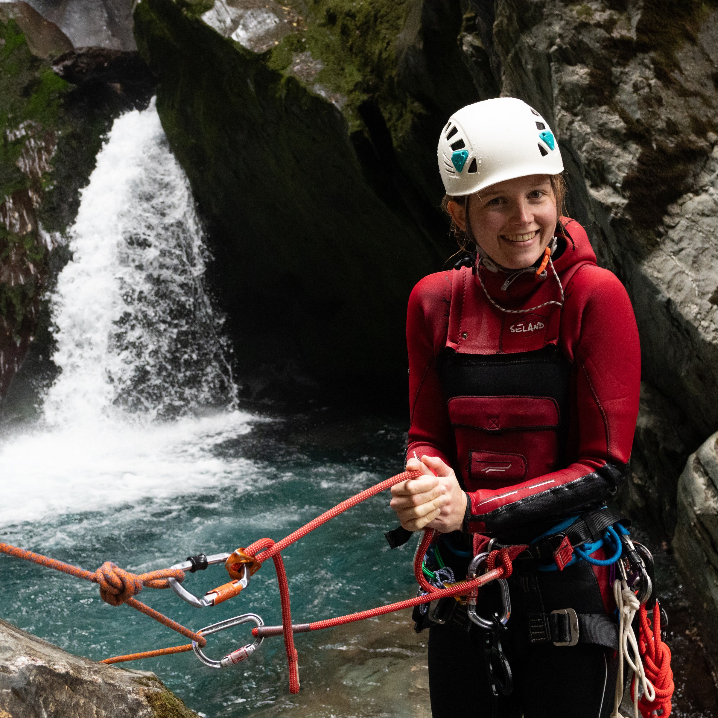 Person in gear smiling while canyoning near a waterfall.