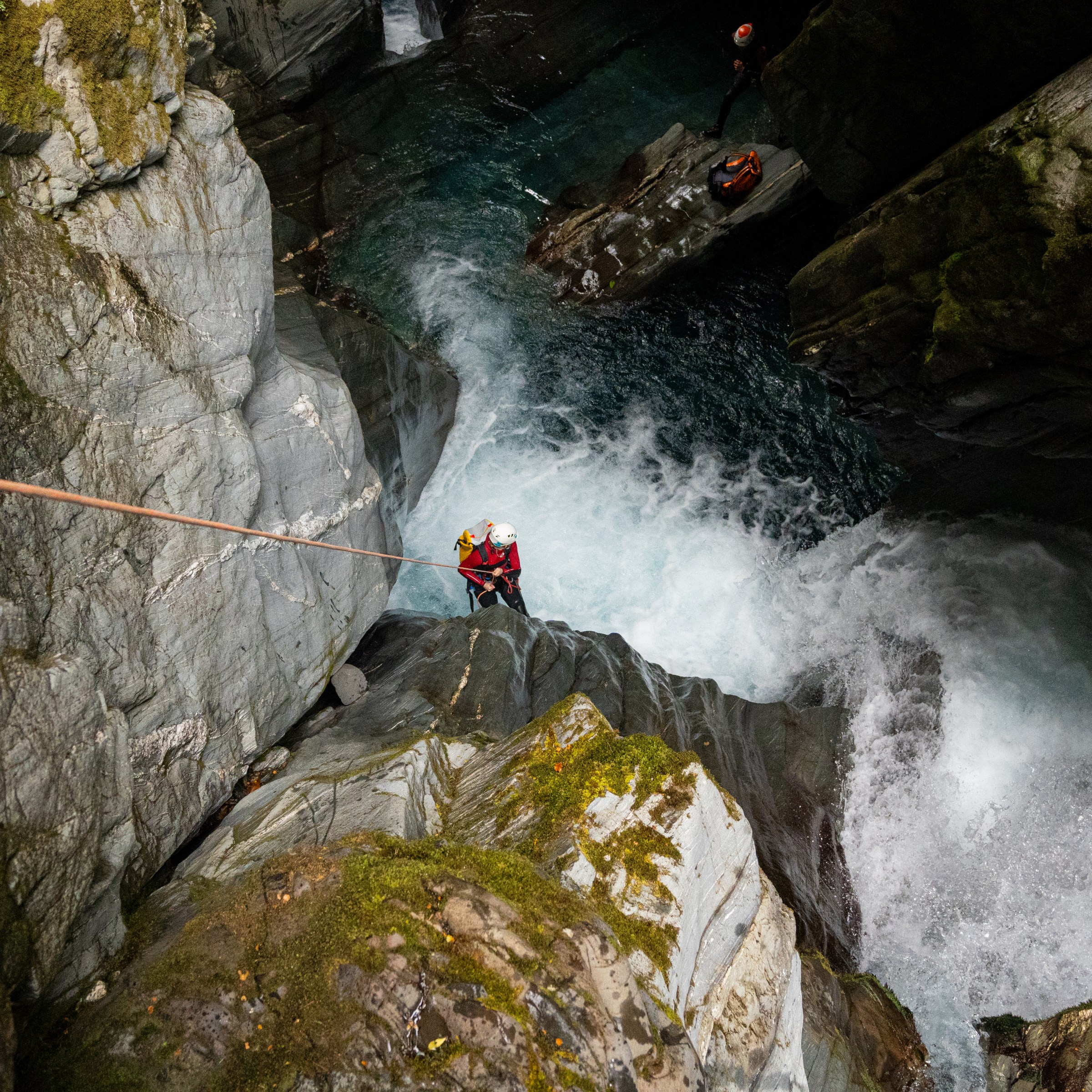 Person canyoning down a waterfall with safety gear on, surrounded by rocky cliffs.