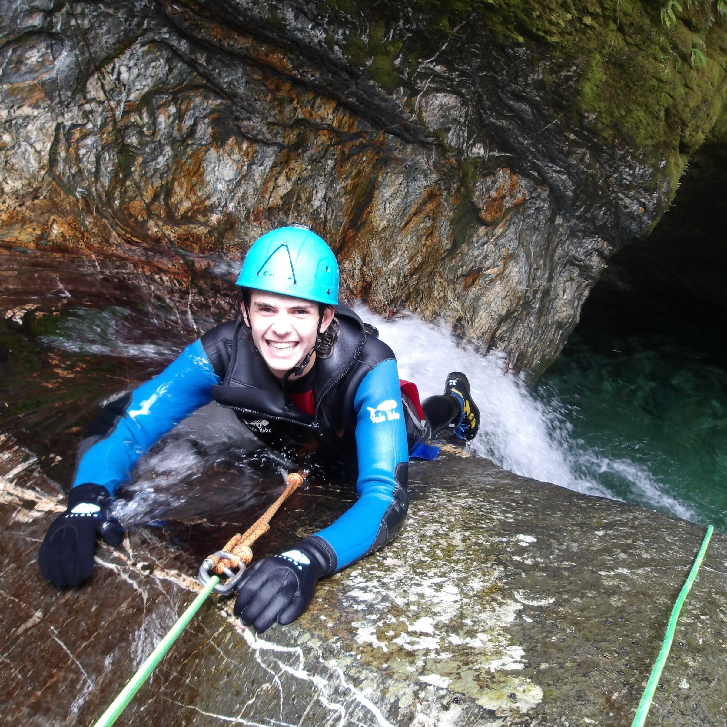 Person in helmet and wetsuit canyoning on a rocky waterfall.